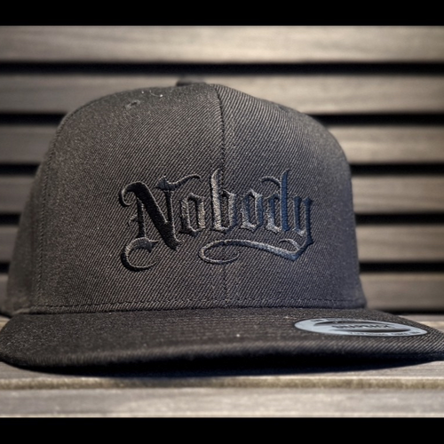 Black cap with 'Naboy' logo on a wooden surface
