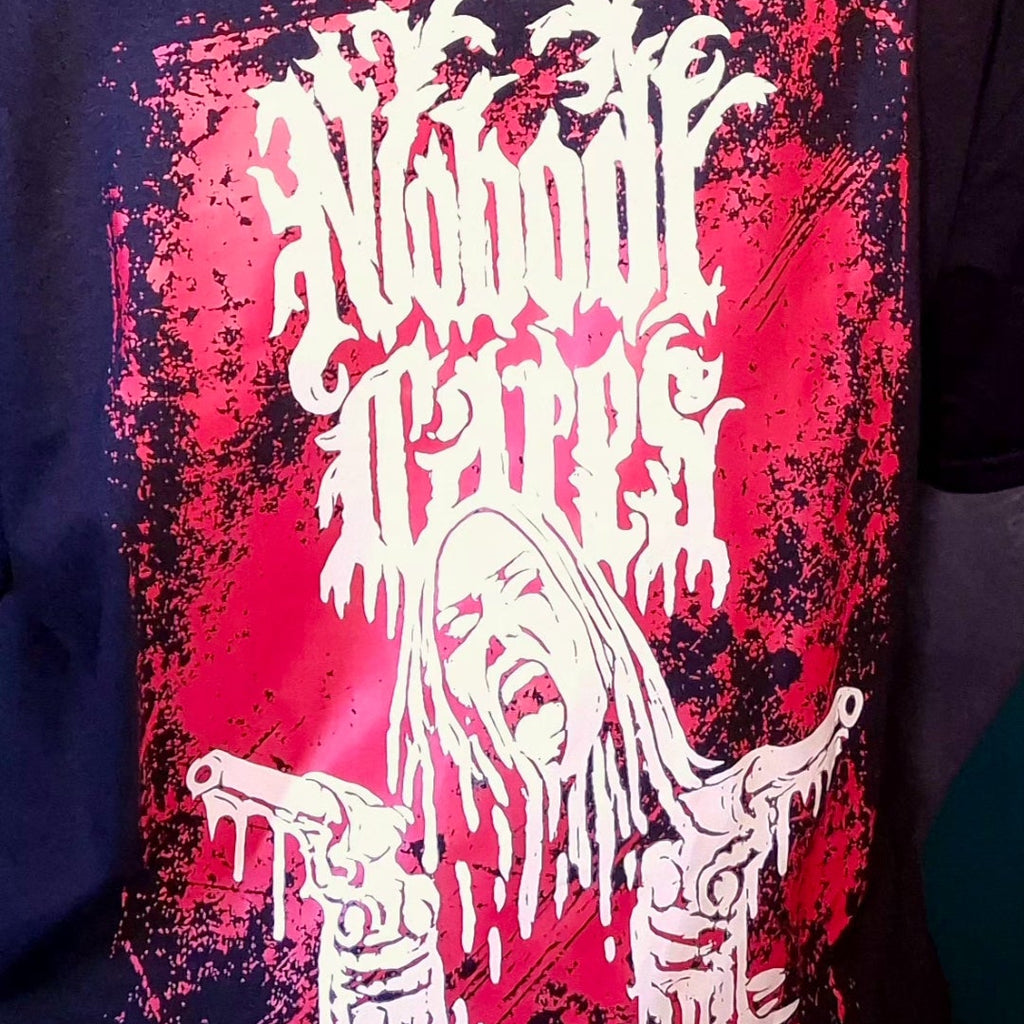 A close-up of a black graphic t-shirt featuring a large red and white horror-style print with the text 'The Nulnool Nether' in a dripping, metallic font above a screaming face and hands holding guns.