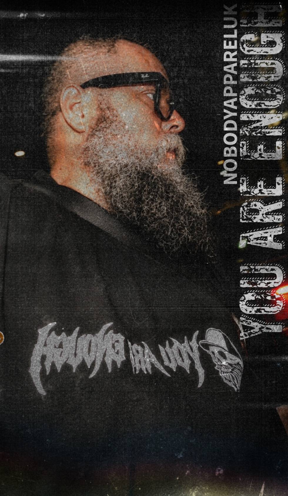 Person wearing a black t-shirt with white text and graphics, standing against a dark background.