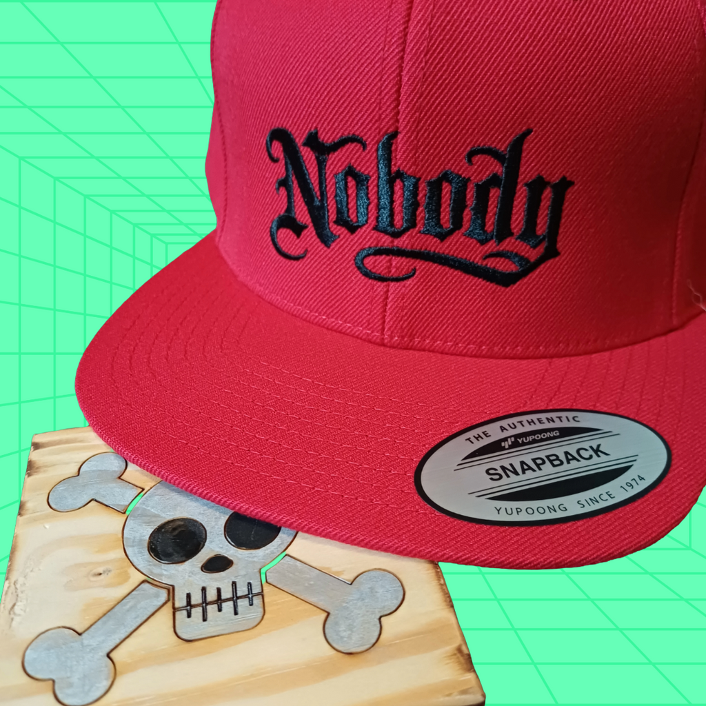 Red snapback cap with 'Nobody' text on a green and blue geometric patterned background