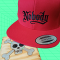 Red snapback cap with 'Nobody' text on a green and blue geometric patterned background