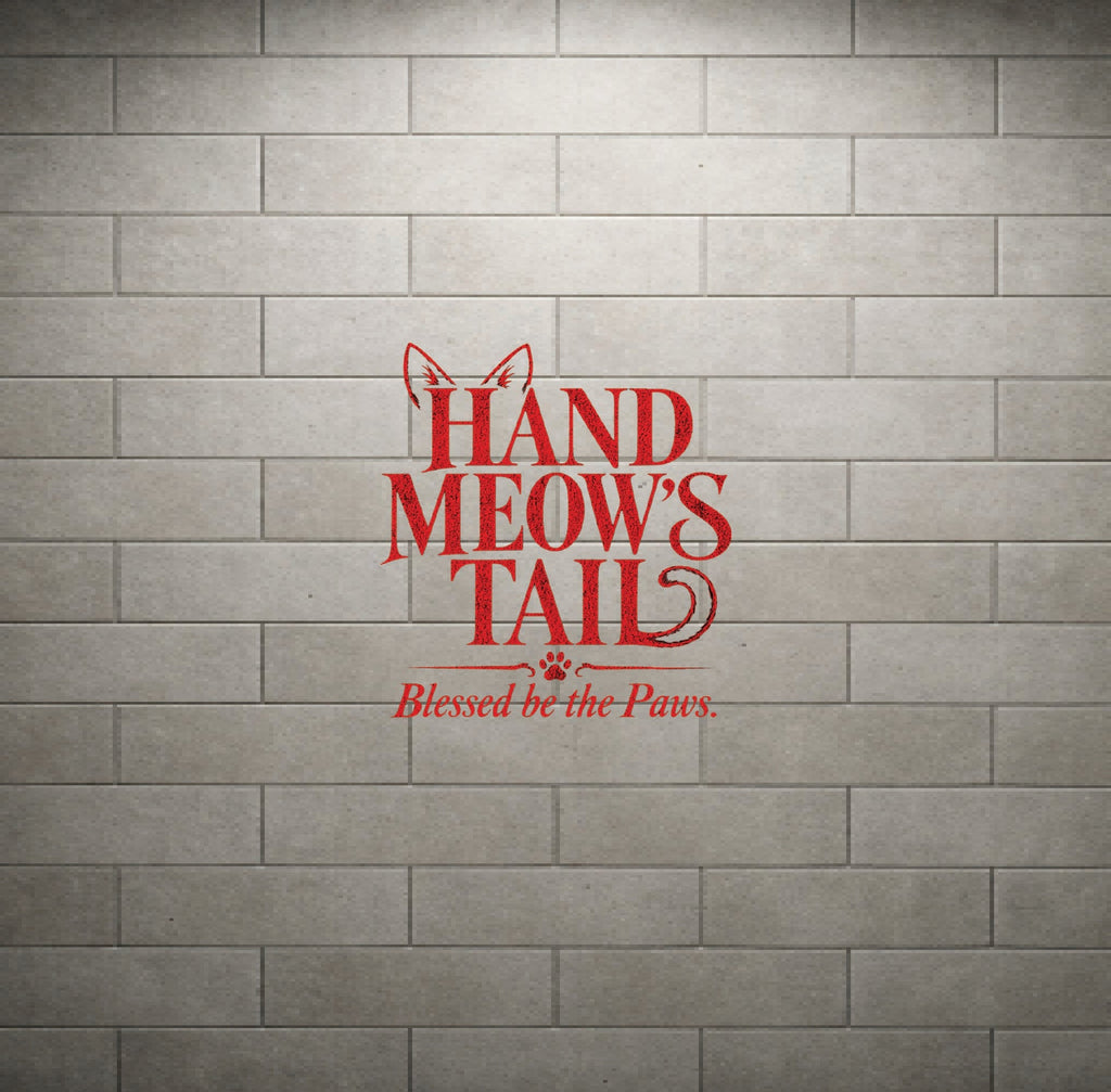 Red vinyl wall decal reading 'HAND MEOW'S TAIL' with 'Blessed be the Paws.' underneath, displayed on a gray brick wall background.