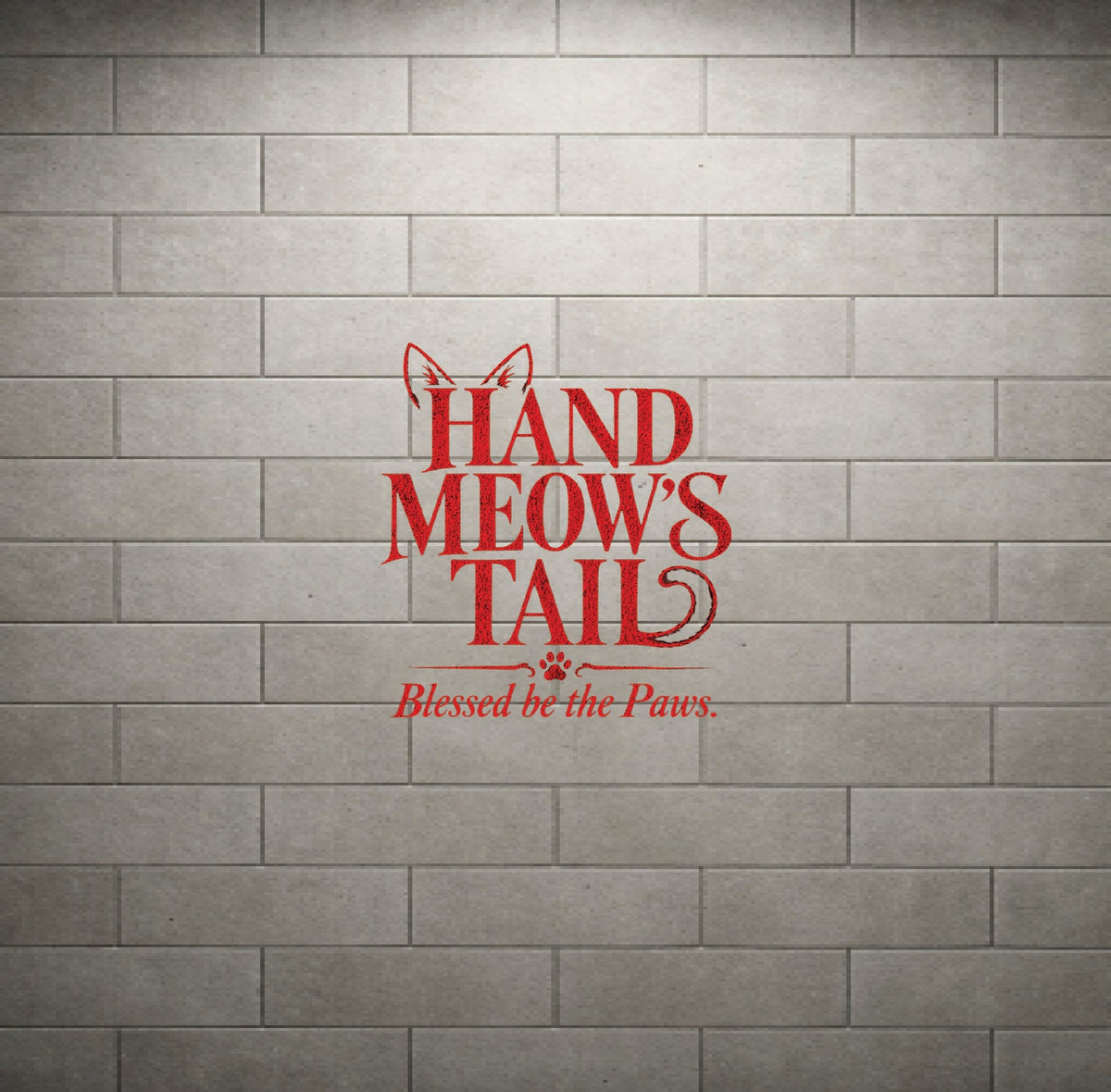 Red vinyl wall decal reading 'HAND MEOW'S TAIL' with 'Blessed be the Paws.' underneath, displayed on a gray brick wall background.