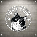 A circular black and white graphic featuring a tuxie cat illustration with the text 'TUXIE CLUB' and paw prints, shown on a gray brick wall background with small paw icons in the corners.